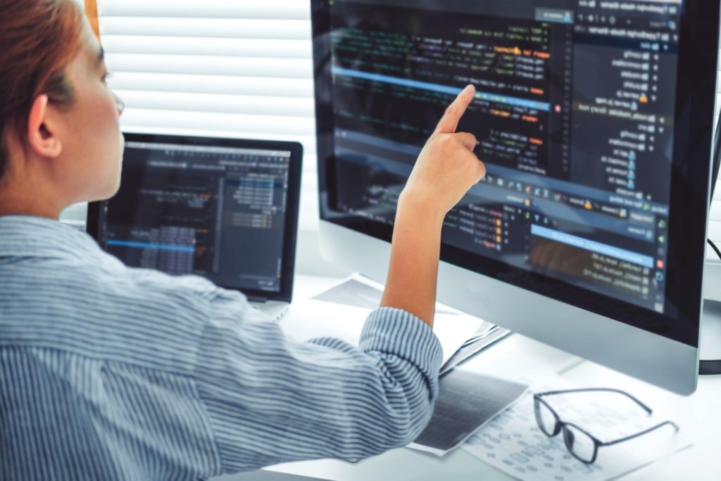 lady pointing towards a desktop computer screen that is showing website code as part of a Web maintenance activity