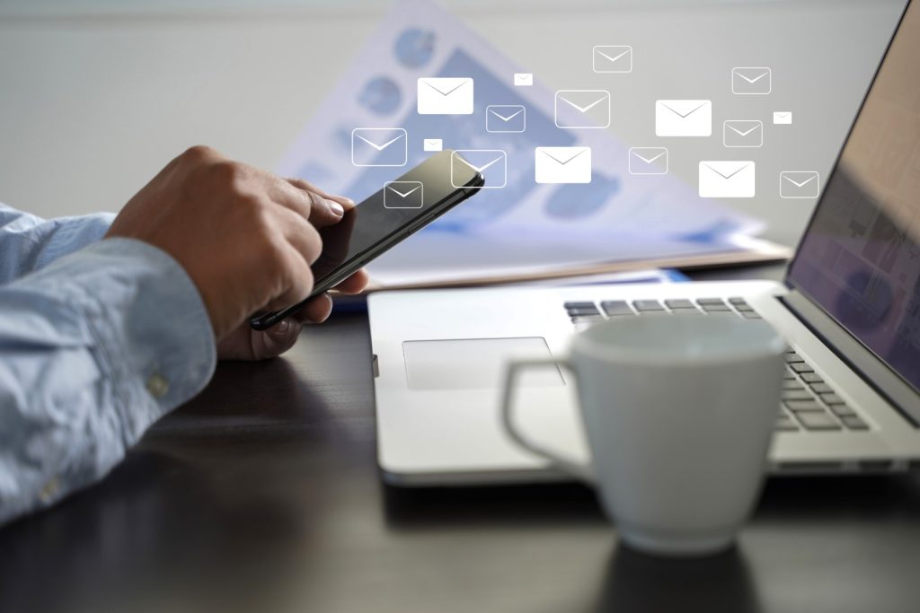 A man sitting working on a laptop and mobile. Digital Marketing specialist working on Email marketing. Virtual Email icons.
