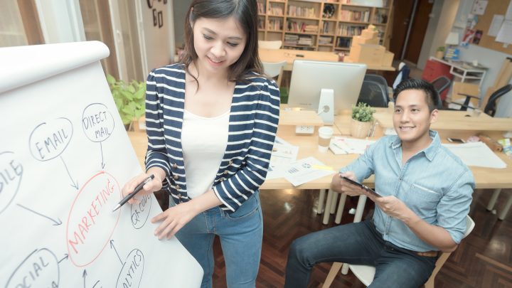 Woman pointing to a chart & explaining Ecommerce marketing elements like Email marketing & social media to her male colleague